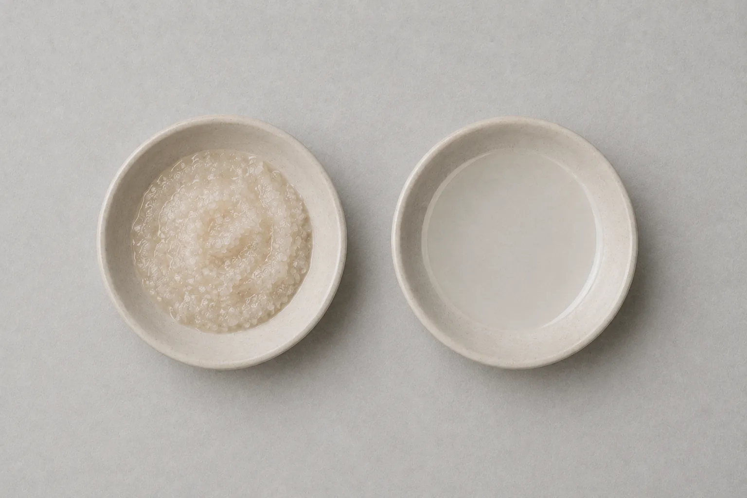 Two small dishes on a plain surface: one holding a coarse, gritty scrub, the other a smooth clear liquid.