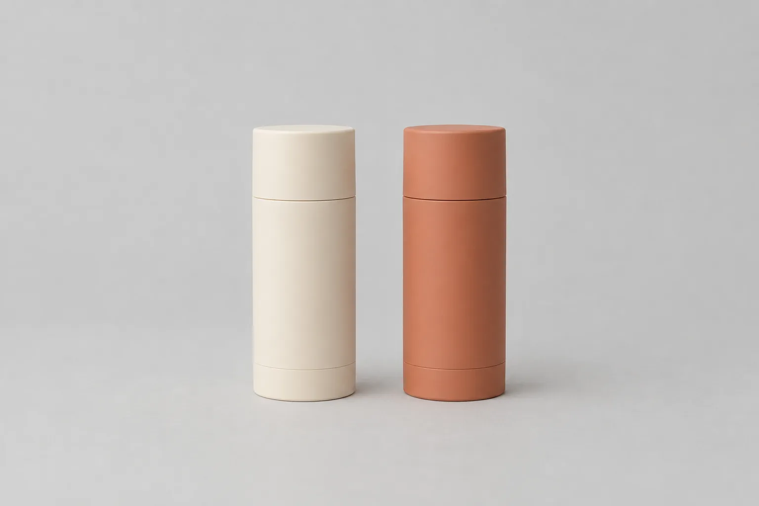 Two plain unbranded deodorant sticks standing side by side, one cream and one terracotta.